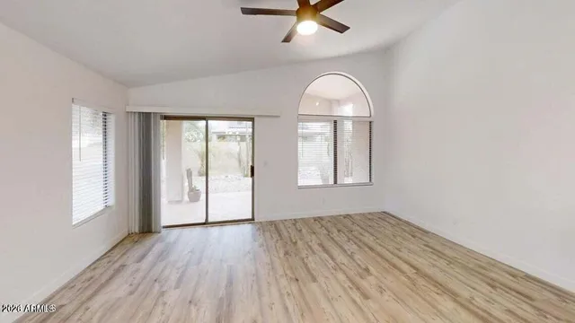 an empty room with wooden floor fan and windows