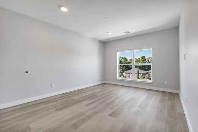 a view of an empty room with wooden floor and window