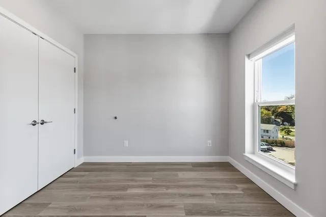 a view of an empty room with wooden floor and a window