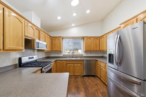 a kitchen with stainless steel appliances granite countertop a refrigerator a sink dishwasher a stove and white cabinets with wooden floor