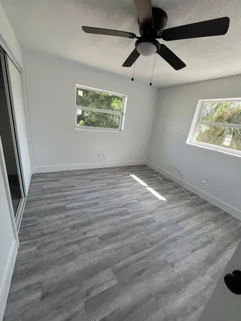 an empty room with wooden floor fan and windows