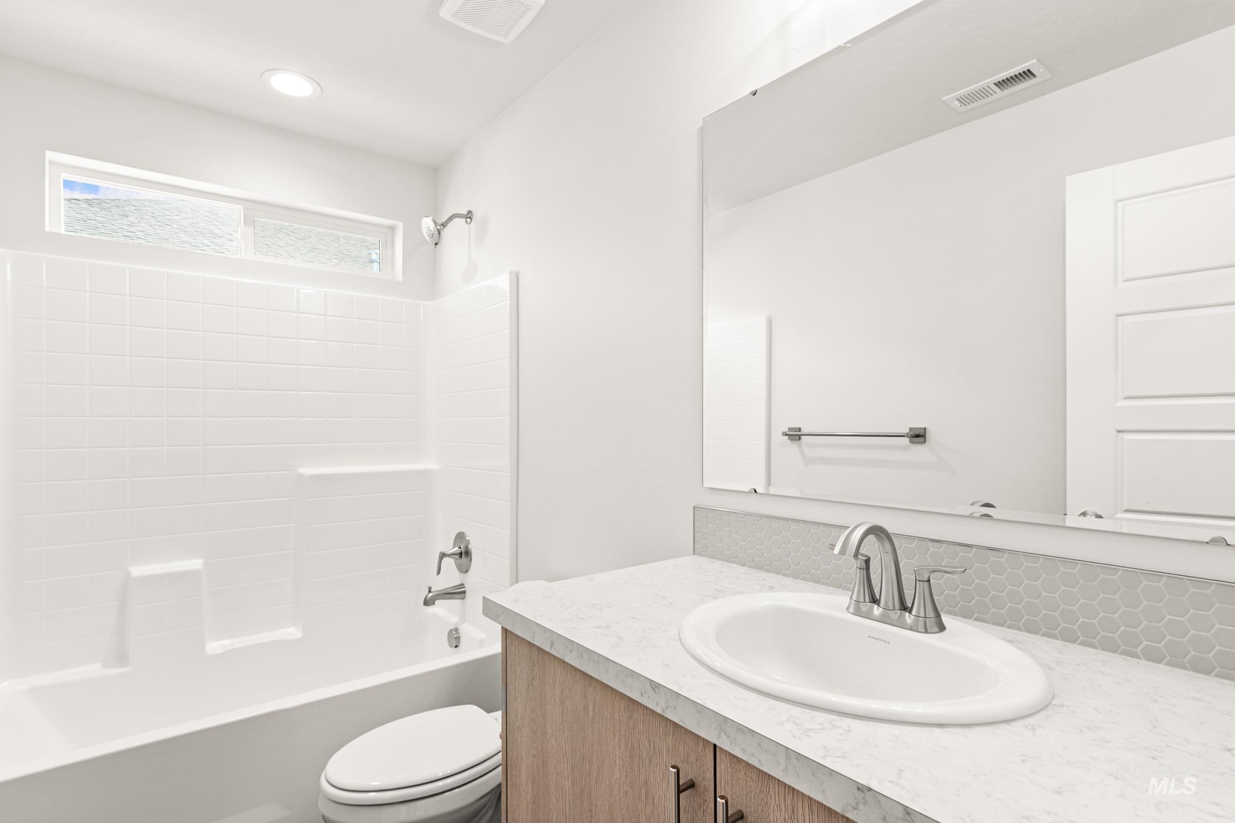 1077 West Jasper Street Meridian, ID 83642 - Photo 13 of 19 Bathroom featuring a white subway tile tub surround with an integrated shower, a white vanity with a light-colored countertop, and a hexagonal tile backsplash