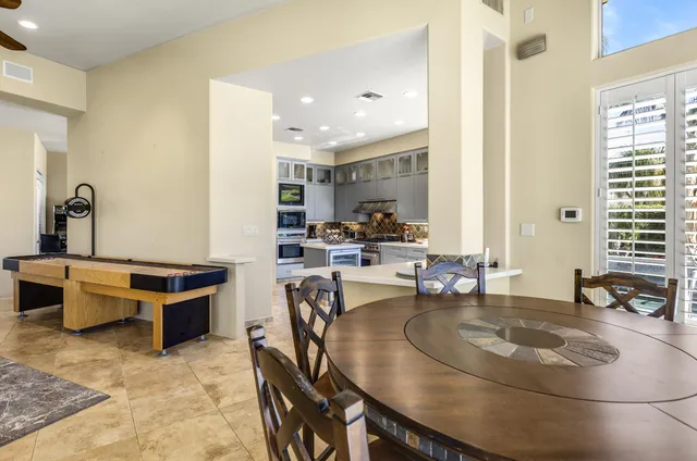 a dining hall with stainless steel appliances kitchen island granite countertop a table chairs and a view of living room