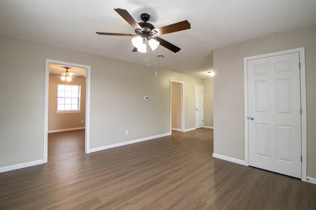 a view of an empty room with wooden floor and a ceiling fan