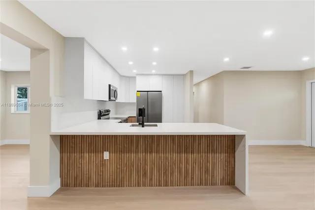 a large white kitchen with kitchen island a sink wooden floor and stainless steel appliances