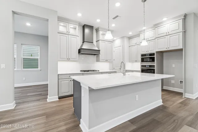 a large kitchen with stainless steel appliances kitchen island granite countertop a stove a sink a refrigerator and white cabinets with wooden floor