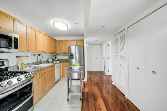 a kitchen with stainless steel appliances a stove top oven a sink a refrigerator white cabinets and wooden floor