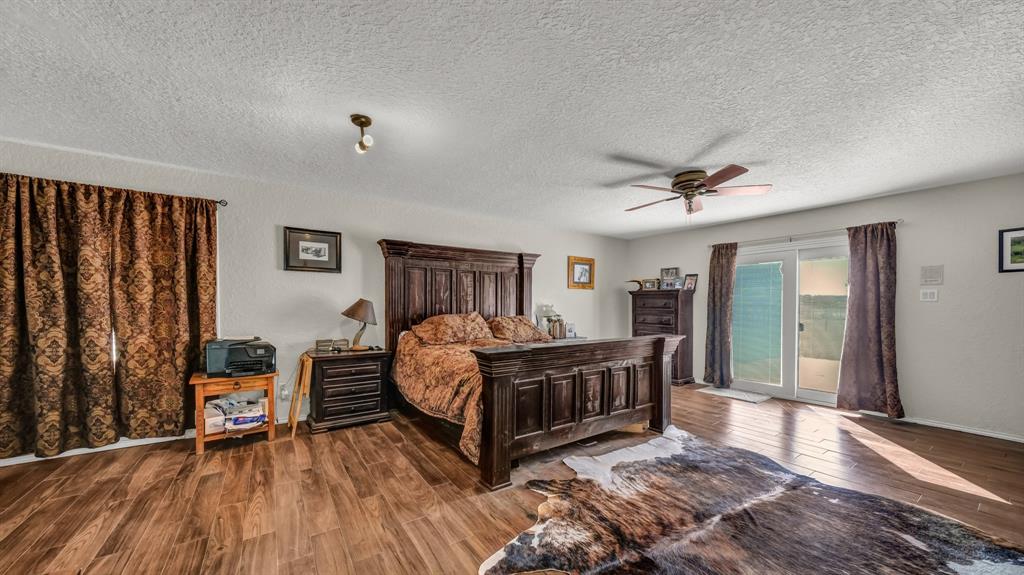 1003 Lamkin Road Mineral Wells, TX 76067 - Photo 9 of 40 Bedroom with wood finished floors, access to outside, a textured ceiling, a ceiling fan, and a textured wall