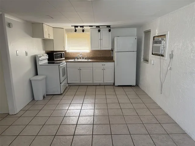 a kitchen with white cabinets a sink a stove a refrigerator and windows