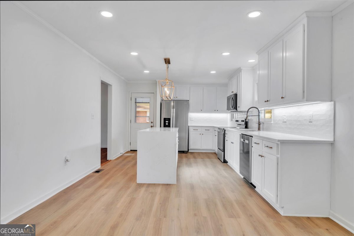 1806 Knox Street Dublin, GA 31021 - Photo 7 of 48 a open kitchen with white cabinets a sink dishwasher a dining table and chairs with wooden floor