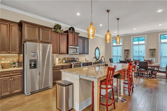 a kitchen with stainless steel appliances a refrigerator a stove a sink a dining table and chairs with wooden floor