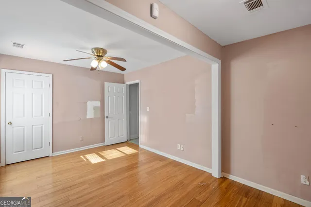 an empty room with wooden floor chandelier fan and windows