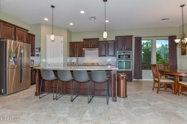 a kitchen with stainless steel appliances granite countertop a table chairs refrigerator and sink
