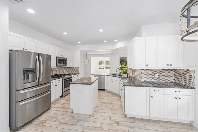 a kitchen with stainless steel appliances kitchen island granite countertop a refrigerator a stove a sink and white cabinets