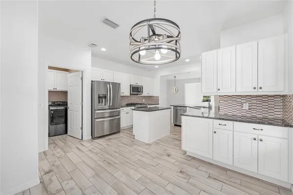 a kitchen with granite countertop a refrigerator a stove and white cabinets with wooden floor