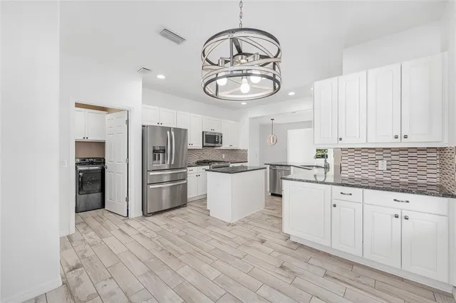 a kitchen with granite countertop a refrigerator a stove and white cabinets with wooden floor