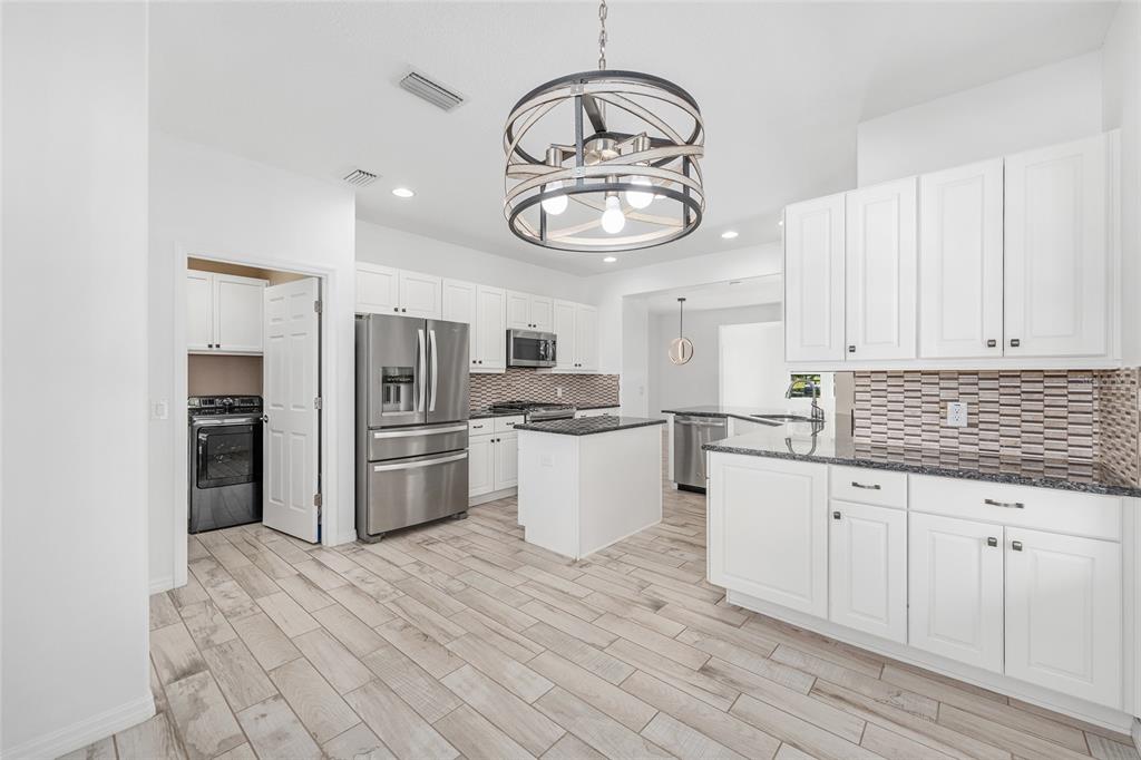 4970 Northwest 35th Ln Road Ocala, FL 34482 - Photo 20 of 41 a kitchen with granite countertop a refrigerator a stove and white cabinets with wooden floor