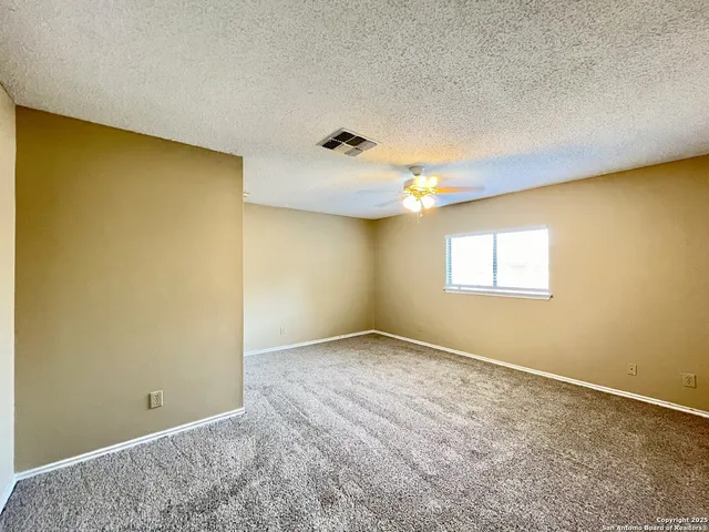an empty room with a chandelier fan and windows