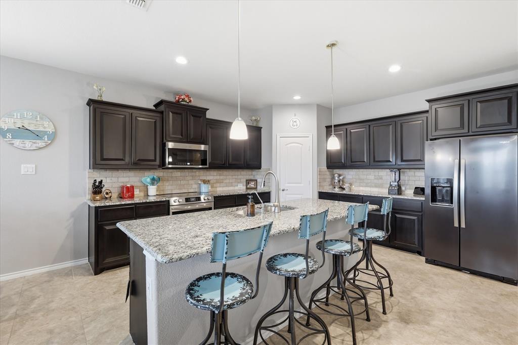11500 Starlight Ranch Fort Worth, TX 76052 - Photo 13 of 40 This kitchen features dark cabinetry, stainless steel appliances, a tile backsplash, and a large island with a light-colored countertop