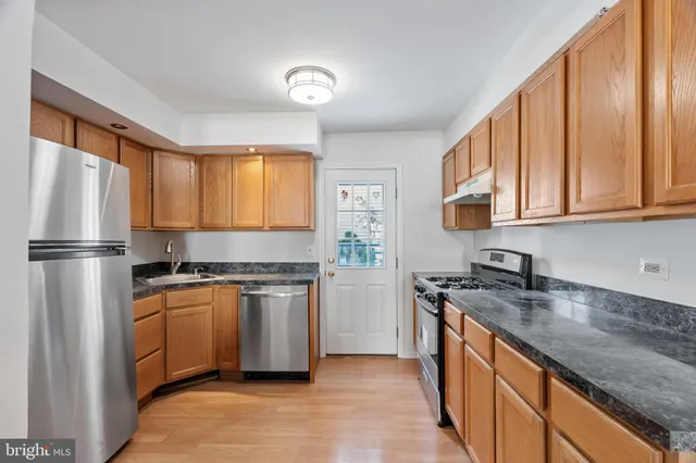 a kitchen with stainless steel appliances granite countertop a stove top oven a refrigerator a sink and dishwasher with wooden floor