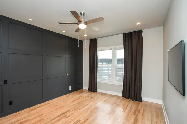 a view of an empty room with wooden floor and a ceiling fan