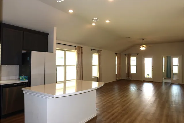 a view of an empty room with wooden floor and a kitchen