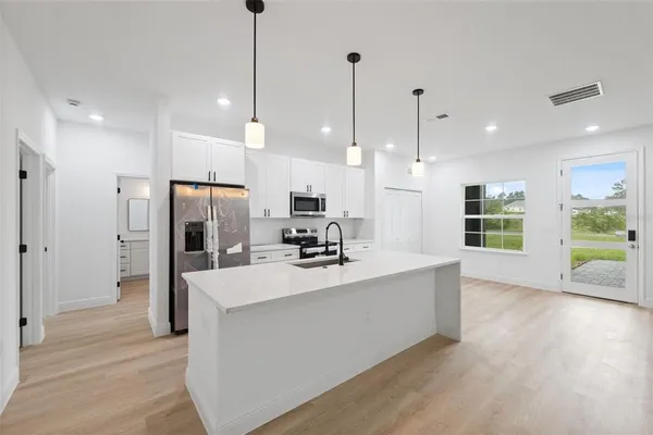 a large kitchen with kitchen island a large counter top a refrigerator and a wooden floor