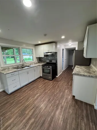 a large kitchen with stainless steel appliances granite countertop a stove a sink dishwasher and a oven with white cabinets