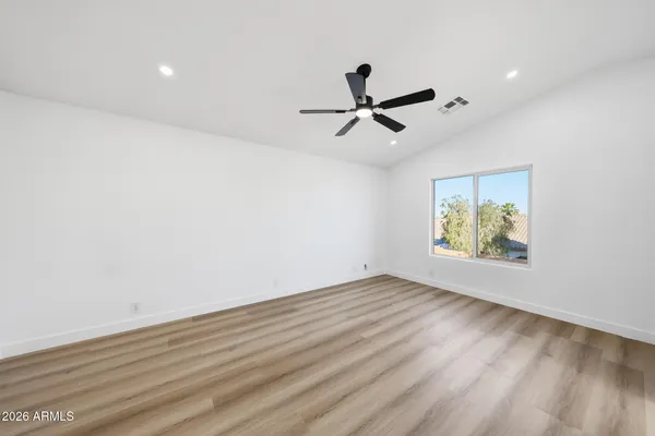 an empty room with wooden floor ceiling fan and windows