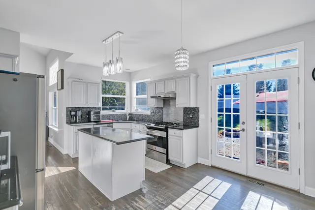 a kitchen with stainless steel appliances granite countertop a refrigerator a stove a sink dishwasher and white cabinets with wooden floor