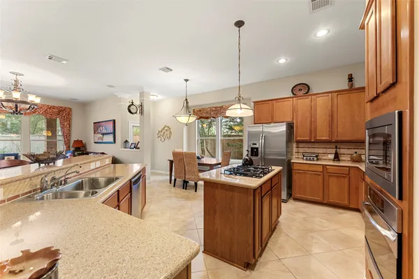 a kitchen with stainless steel appliances granite countertop a stove top oven a refrigerator a sink and chairs