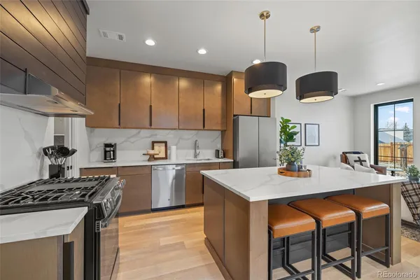 a kitchen with stainless steel appliances granite countertop a stove top oven a sink a dining table and chairs with wooden floor