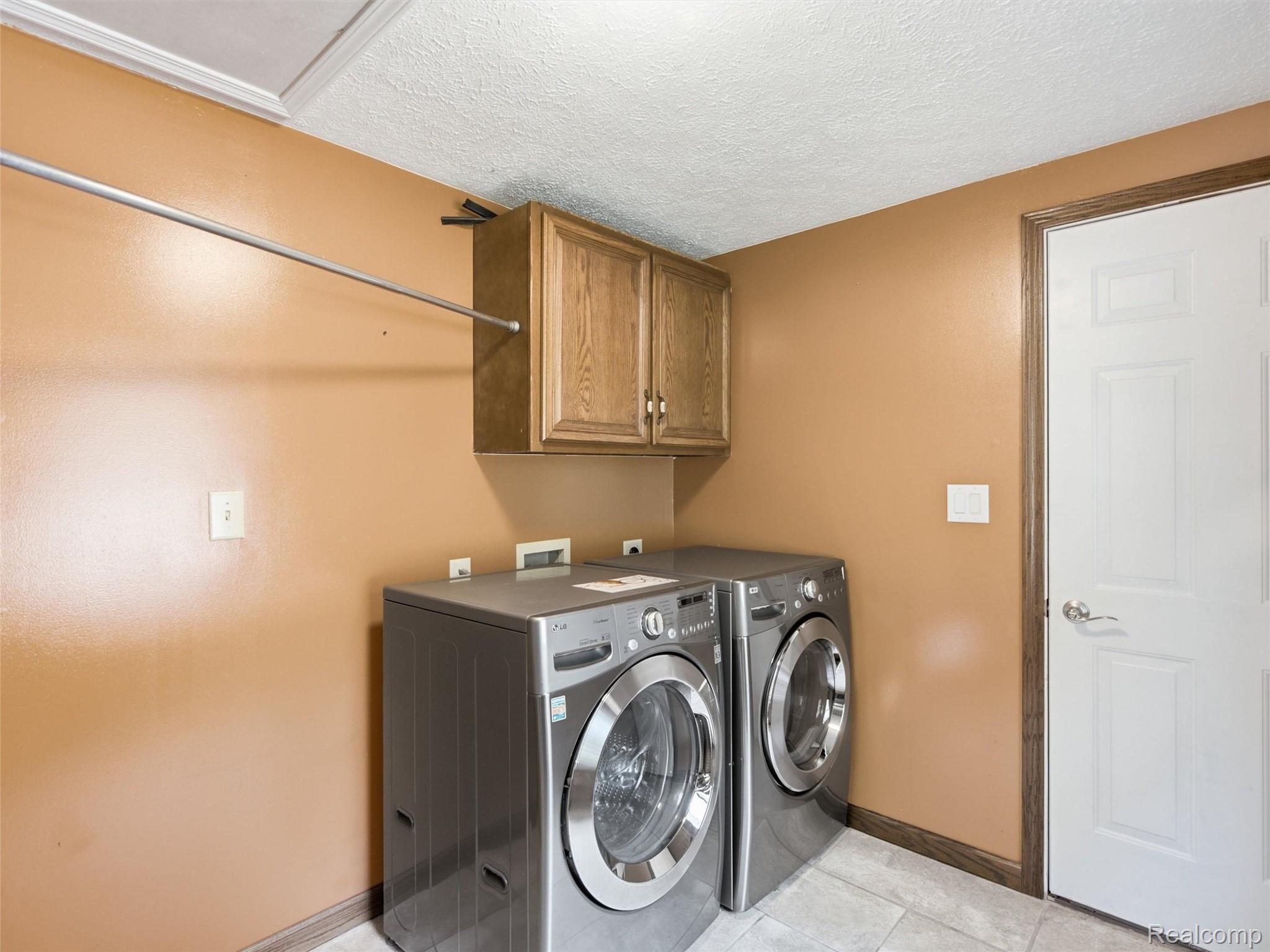 5003 Mason Road Howell, MI 48843 - Photo 16 of 59 Laundry area featuring wood-finish cabinetry, a white paneled door with brushed nickel hardware, and tile flooring