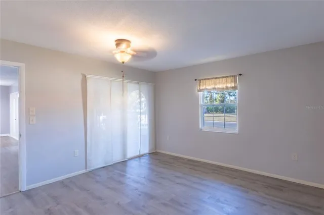 an empty room with wooden floor chandelier fan and windows