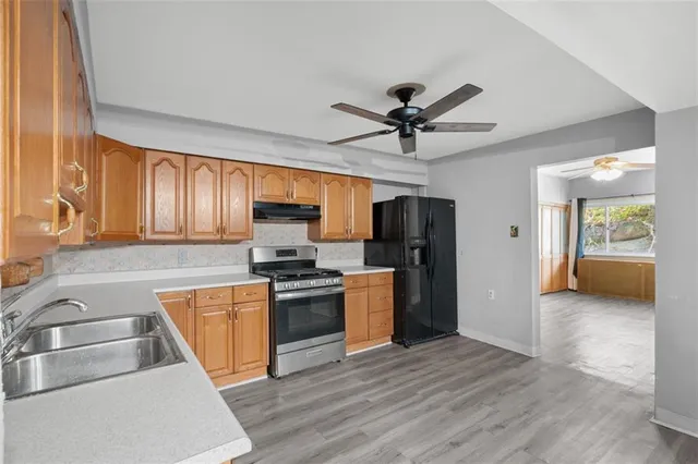 a kitchen with stainless steel appliances granite countertop a sink a stove a refrigerator cabinets and a dining table with wooden floor