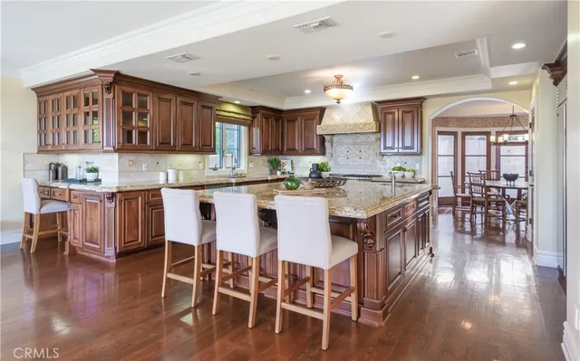 a kitchen with stainless steel appliances granite countertop a stove top oven a sink a dining table and chairs with wooden floor