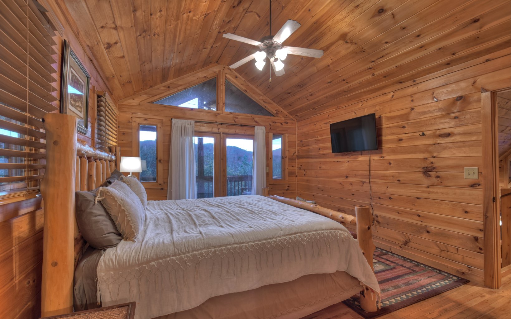 216 The Forest Road Blue Ridge, GA 30513 - Photo 34 of 41 a bedroom with a large bed a flat tv screen and a chandelier
