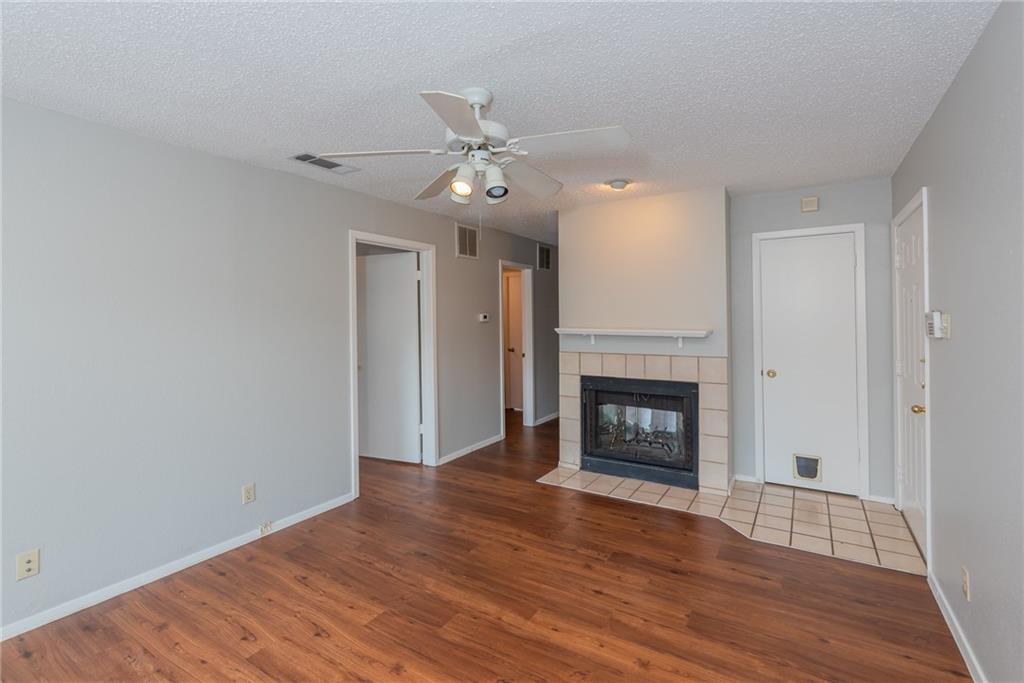 3115 Helms Street, Unit 116 Austin, TX 78705 - Photo 2 of 12 Unfurnished living room with ceiling fan, light wood finished floors, a tiled fireplace, and a textured ceiling