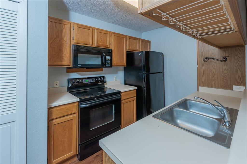 3115 Helms Street, Unit 116 Austin, TX 78705 - Photo 6 of 12 Kitchen featuring black appliances, light countertops, wood finish cabinets, wood finished floors, and a textured ceiling
