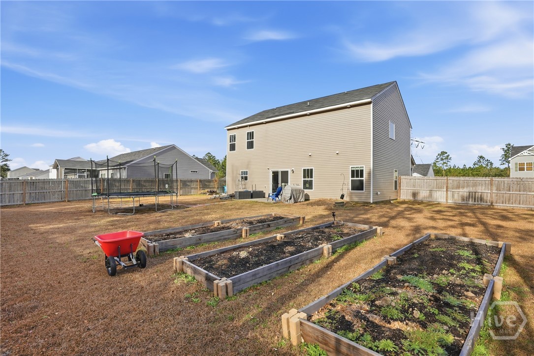 313 Crosswinds Drive Rincon, GA 31326 - Photo 30 of 34 Spacious fenced backyard with raised garden beds, dry lawn, and a two-story beige house.