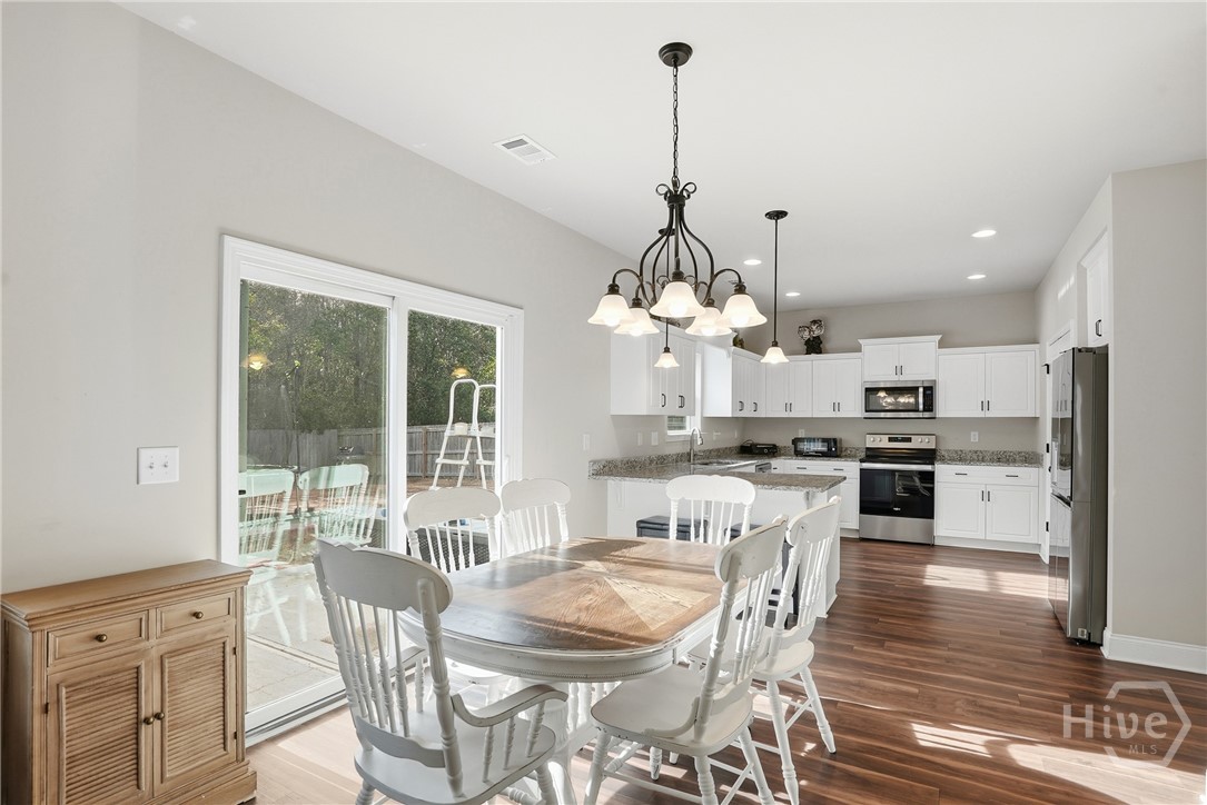 313 Crosswinds Drive Rincon, GA 31326 - Photo 7 of 34 Bright open-concept kitchen and dining area with white cabinetry, granite countertops, wood flooring, farmhouse-style dining set, modern light fixtures, and sliding glass doors leading to a backyard deck.