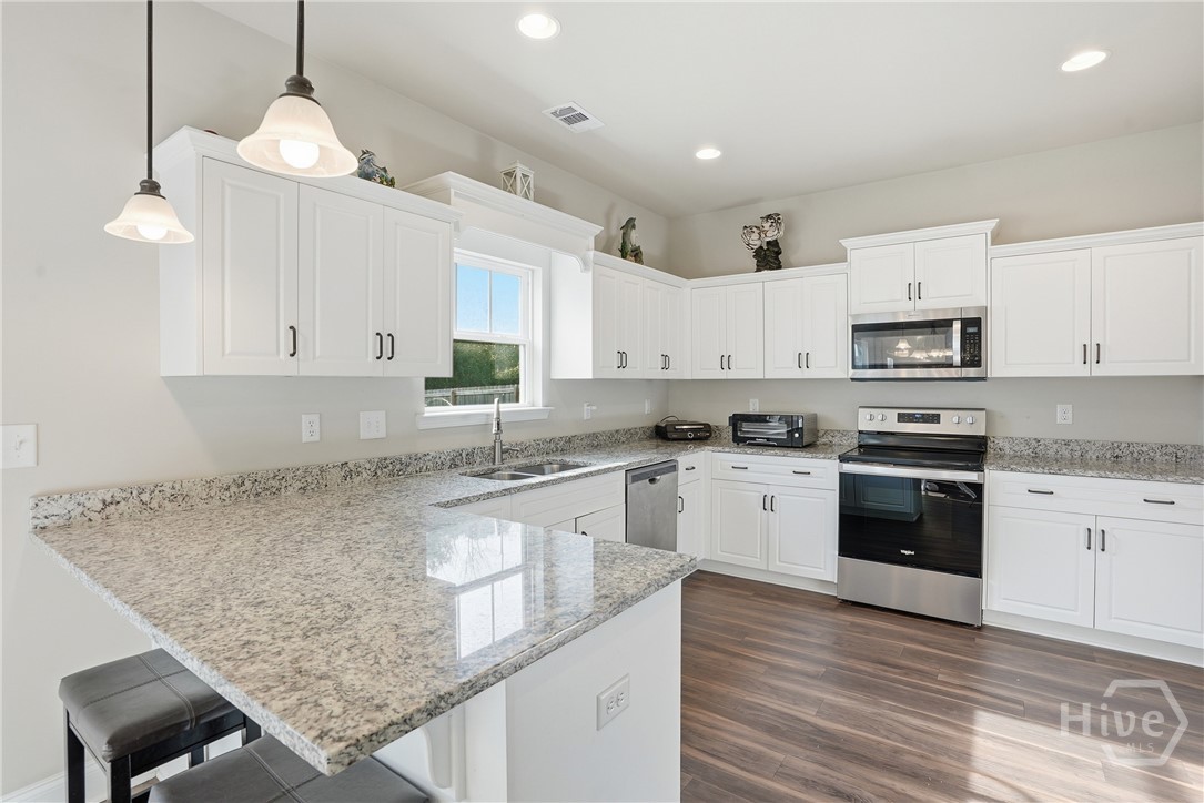 313 Crosswinds Drive Rincon, GA 31326 - Photo 9 of 34 Modern kitchen interior featuring white shaker cabinets, granite countertops, stainless steel appliances, under-cabinet lighting, wood-look flooring, and a large peninsula with bar seating.