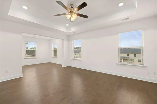 an empty room with wooden floor chandelier fan and windows