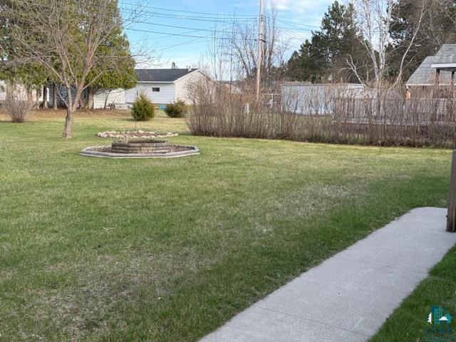 50 Beech Circle Babbitt, MN 55706 - Photo 22 of 24 Expansive grassy yard featuring a central stone-ringed planting area, mature trees, and a concrete pathway