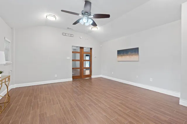 an empty room with wooden floor chandelier fan and windows