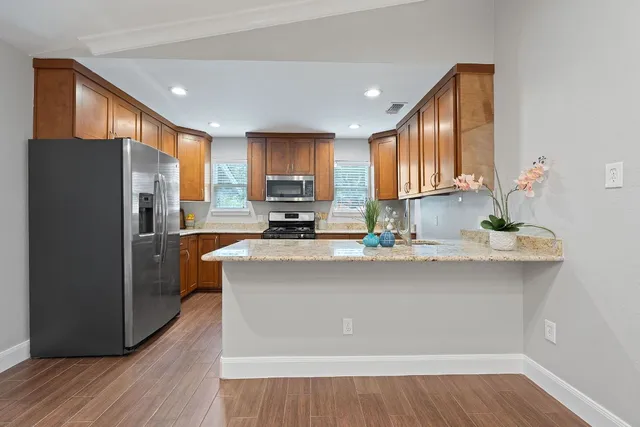 a kitchen with stainless steel appliances granite countertop a refrigerator a sink a stove a microwave and wooden floors