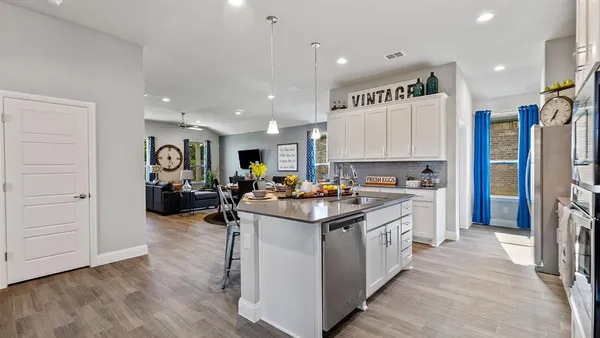 a kitchen with stainless steel appliances kitchen island granite countertop a refrigerator a stove a sink and white cabinets with wooden floor