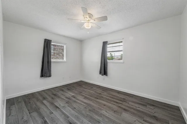 an empty room with wooden floor chandelier fan and windows