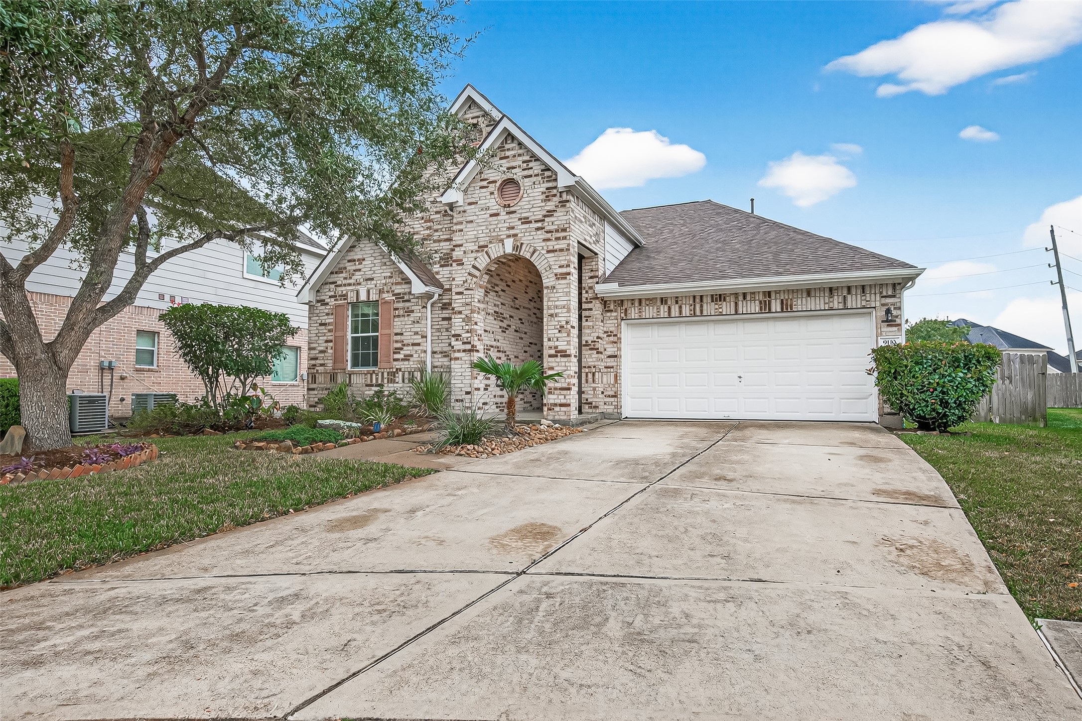 Charming brick home with a two-car garage and a spacious driveway. The front yard features mature trees and well-maintained landscaping, offering great curb appeal.