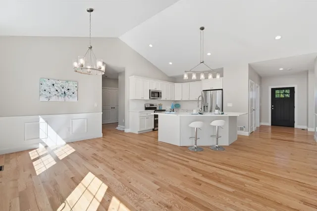 a view of a kitchen with kitchen island stainless steel appliances wooden floor dining table and a chandelier